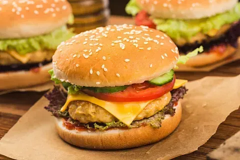 Tres hamburguesas cubiertas con semillas de sésamo, con lechuga, tomate, queso y una hamburguesa reposan sobre papel marrón.