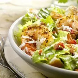 Primer plano de un tazón blanco lleno de ensalada César de salmón, lechuga romana y tocino.