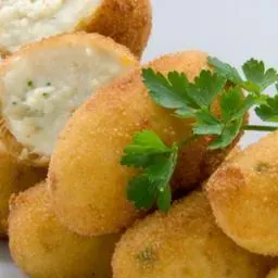 Croquetas doradas y fritas, una de las cuales se abre para revelar un relleno cremoso y se adorna con perejil.