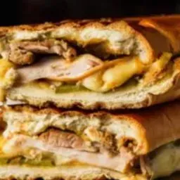 Un primer plano de dos sándwiches cubanos apilados uno encima del otro, mostrando capas de carne, queso y pepinillos.