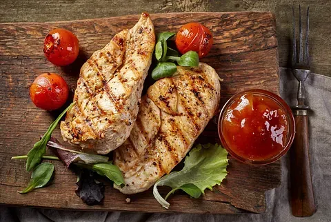 Pechugas de pollo a la plancha con tomates cherry y salsa sobre una tabla de madera, con un tenedor.