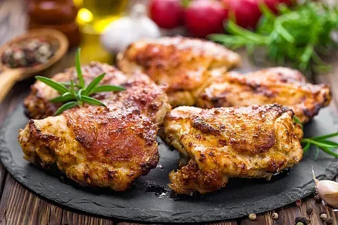 Muslos de pollo a la parrilla sobre una pizarra negra, adornados con romero y ajo. Piel dorada y crujiente.