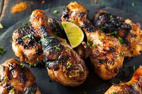 Muslos de pollo a la parrilla en una bandeja de pizarra, con una rodaja de lima. El pollo está carbonizado y reluciente.