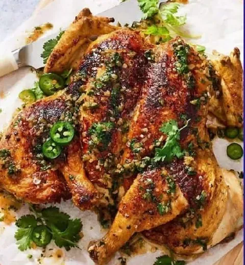 Pollo asado con una sabrosa salsa de hierbas y jalapeño, adornado con cilantro fresco y rodajas de pimienta, servido en papel pergamino.