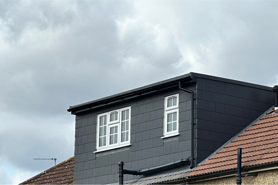 Le toit d'une maison avec une fenêtre dessus et un ciel nuageux en arrière-plan.
