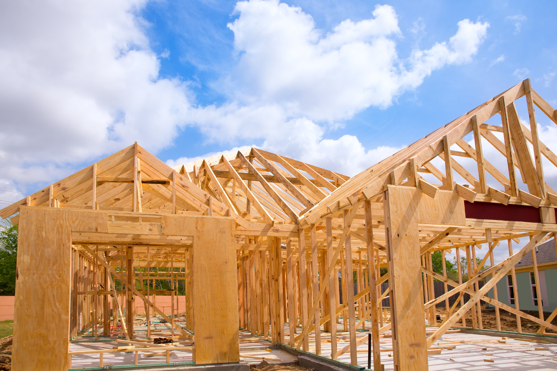 Une maison est en construction avec des poutres en bois et un ciel bleu en arrière-plan.