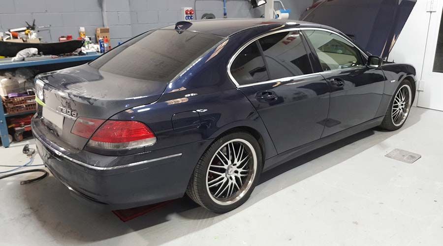 BMW sedán azul oscuro con el capó abierto, estacionado dentro de un garaje.