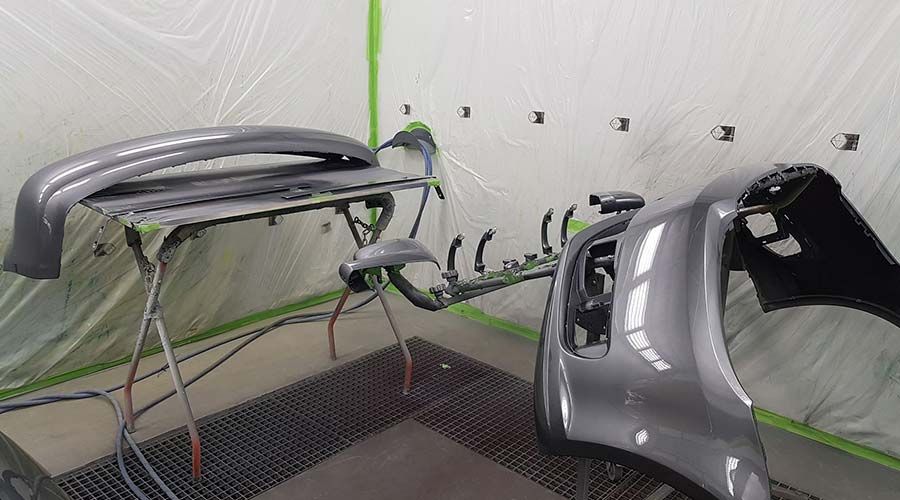 Piezas de automóviles, incluidos parachoques, pintadas con aerosol en una cabina de pintura; colores gris y negro.