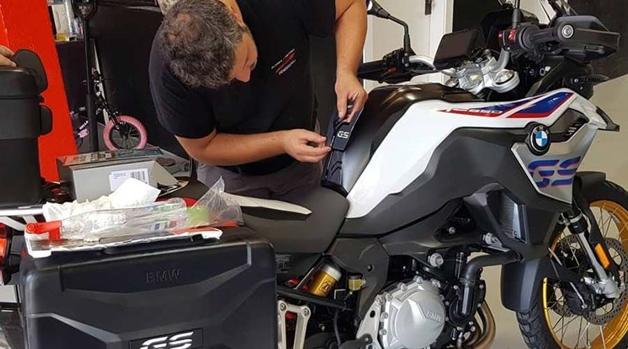 Una persona trabaja en una motocicleta BMW, sentada en el asiento, ajustando algo cerca del depósito de combustible. Se ve una caja negra.