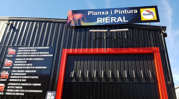 Exterior de un taller mecánico con fachada negra, molduras rojas y un cartel que dice 