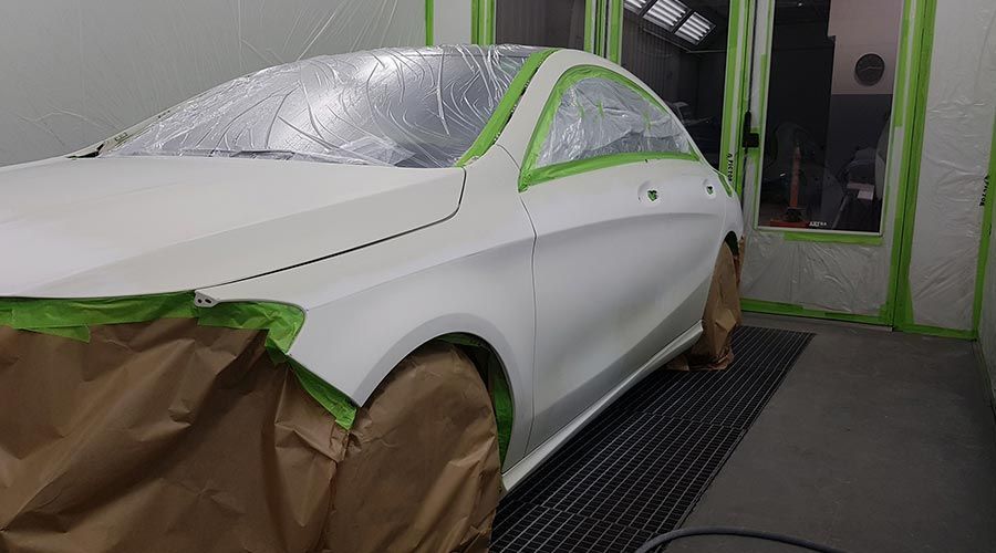 Un coche blanco en una cabina de pintura, enmascarado y listo para pintar. La cinta verde delimita la zona de pintura.