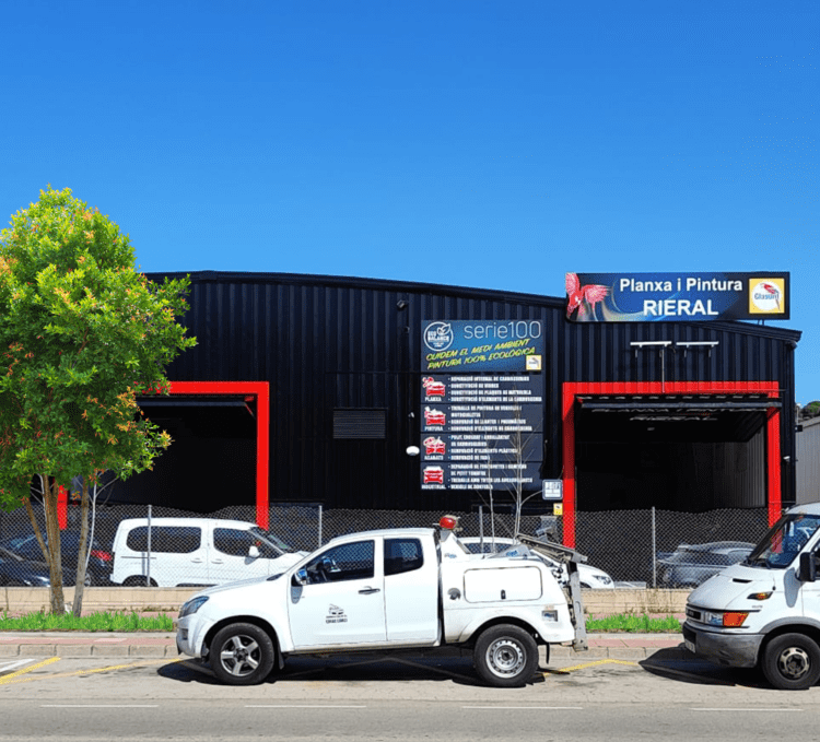 Una camioneta blanca estacionada frente a un edificio negro con detalles en rojo y un cartel que dice 