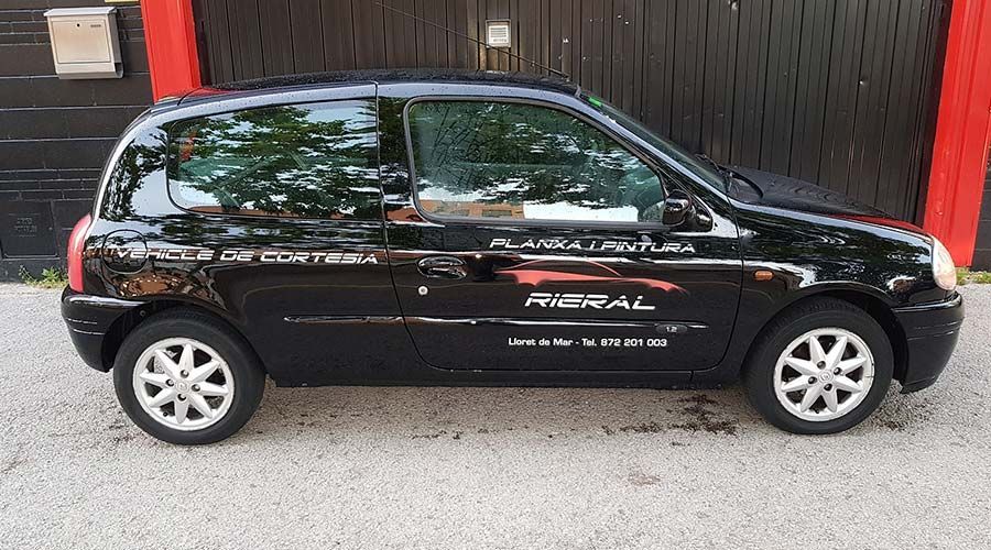 Renault Clio negro aparcado delante de un garaje con logotipos de la empresa en el lateral.