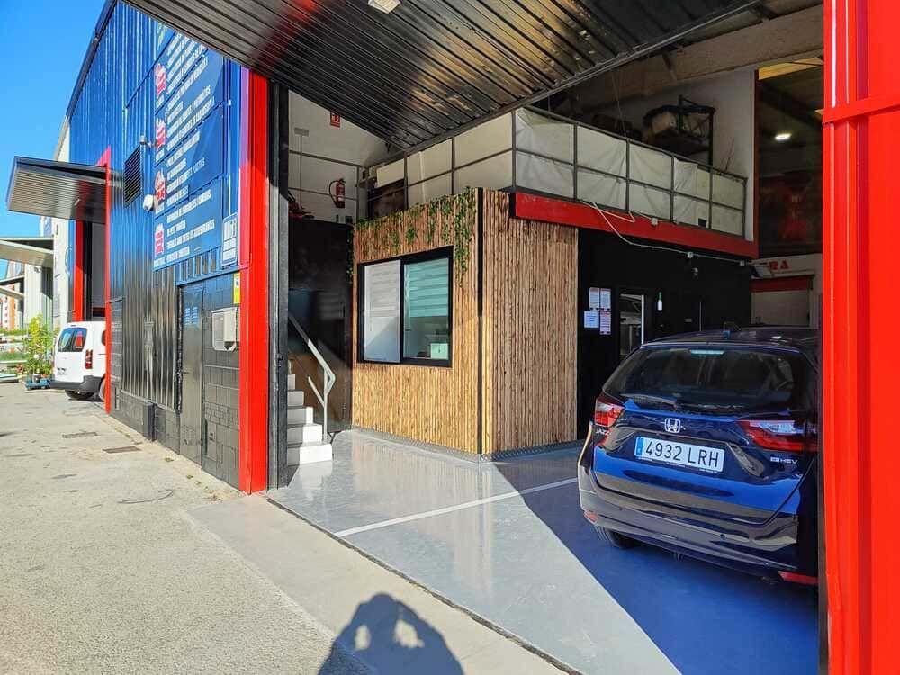 Exterior de un taller mecánico con un coche negro aparcado cerca. El edificio tiene una fachada roja y negra.