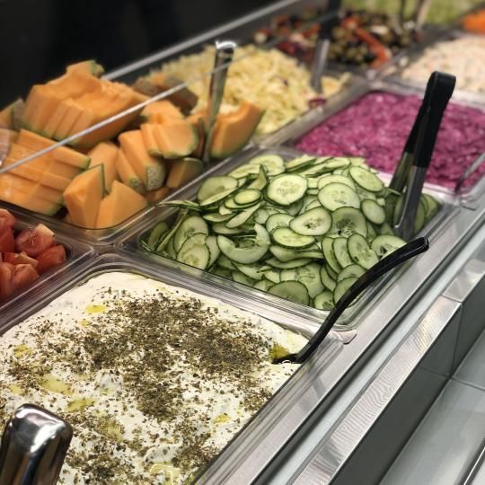 Salaattibuffetissa on viipaloituja kurkkuja, cantaloupea, punasipulia ja maustettua valkoista salaattia metallitarjottimilla