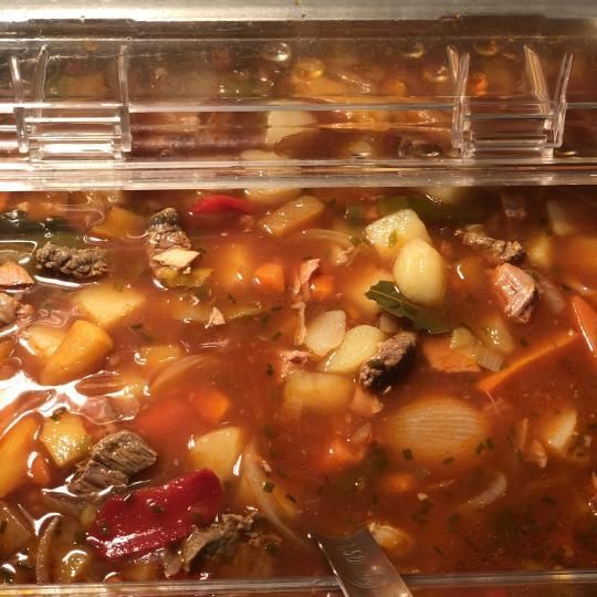 Lähikuva tarjottimella olevasta keitosta, jossa on vihanneksia ja lihaa punertavassa liemessä