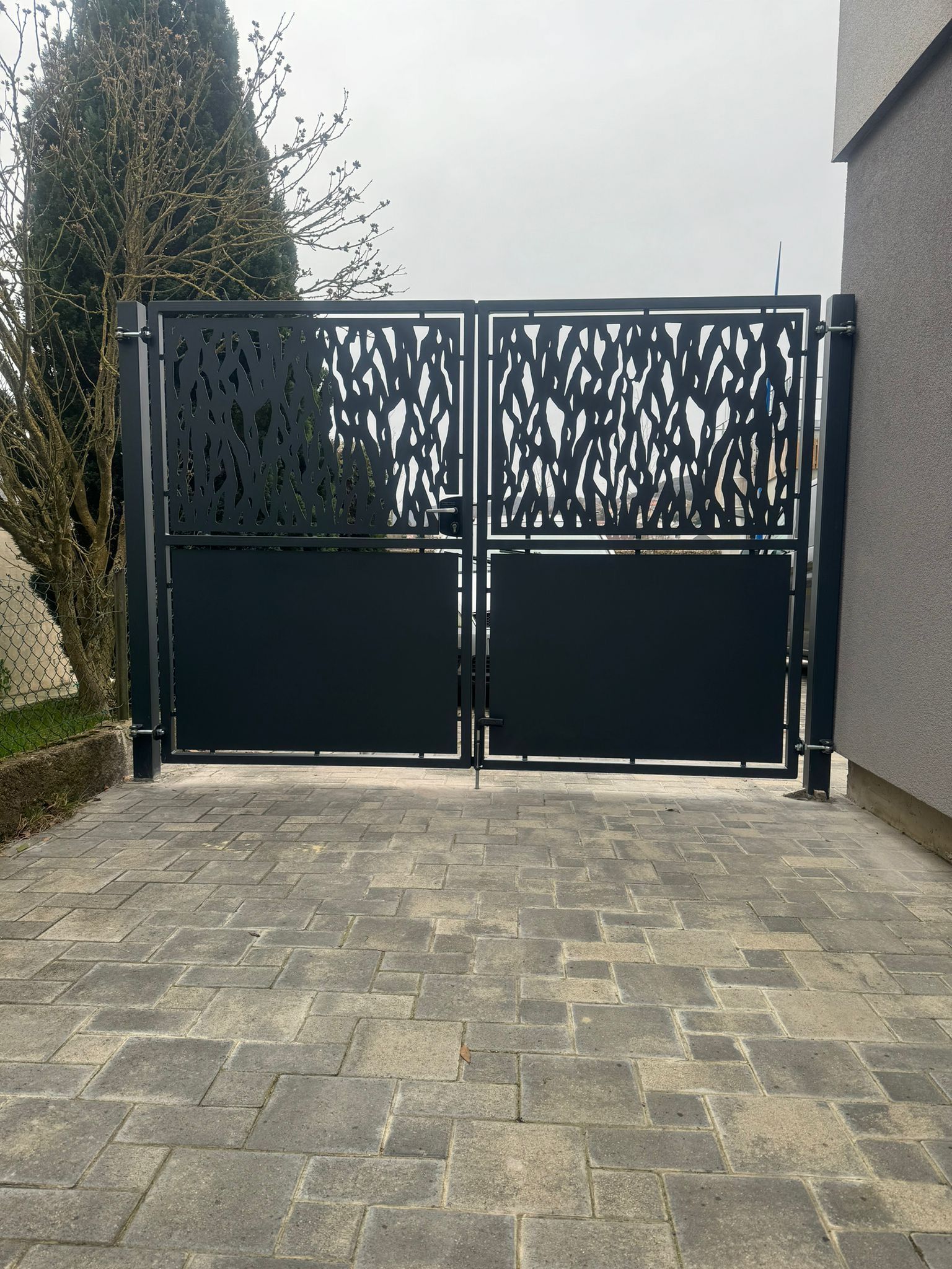 Portail d'allée en métal noir avec panneaux supérieurs décoratifs sur une allée pavée de briques.