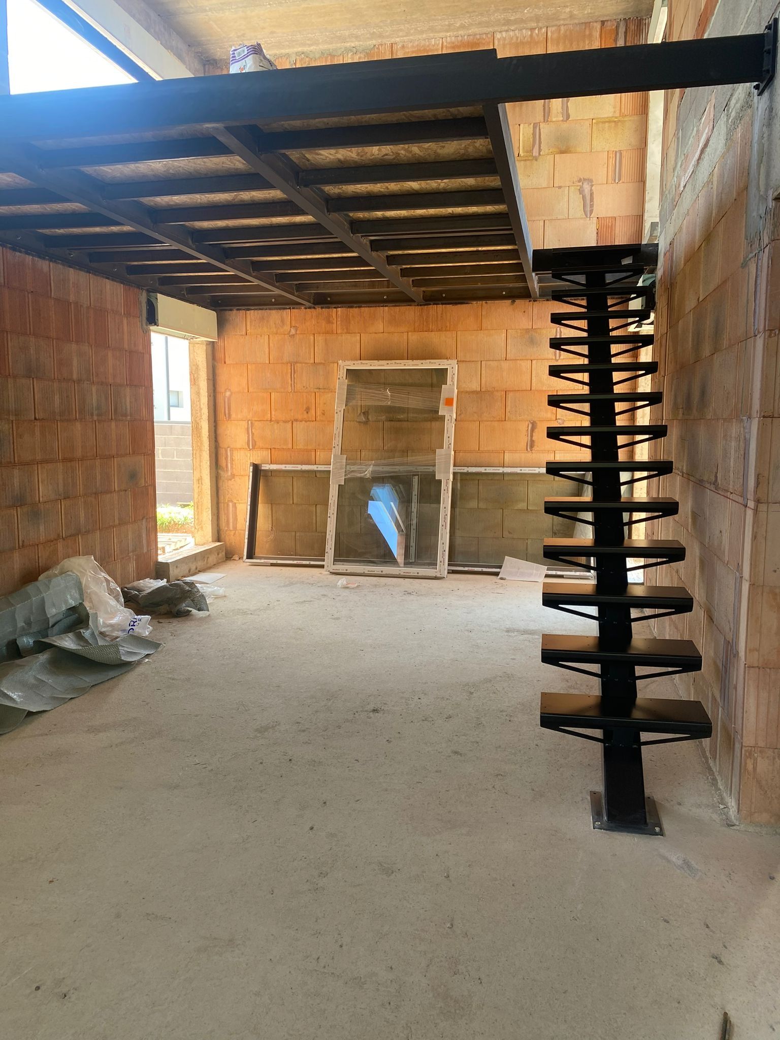 Chantier de construction intérieur : murs en briques, sol en béton, escalier métallique, mezzanine en bois.