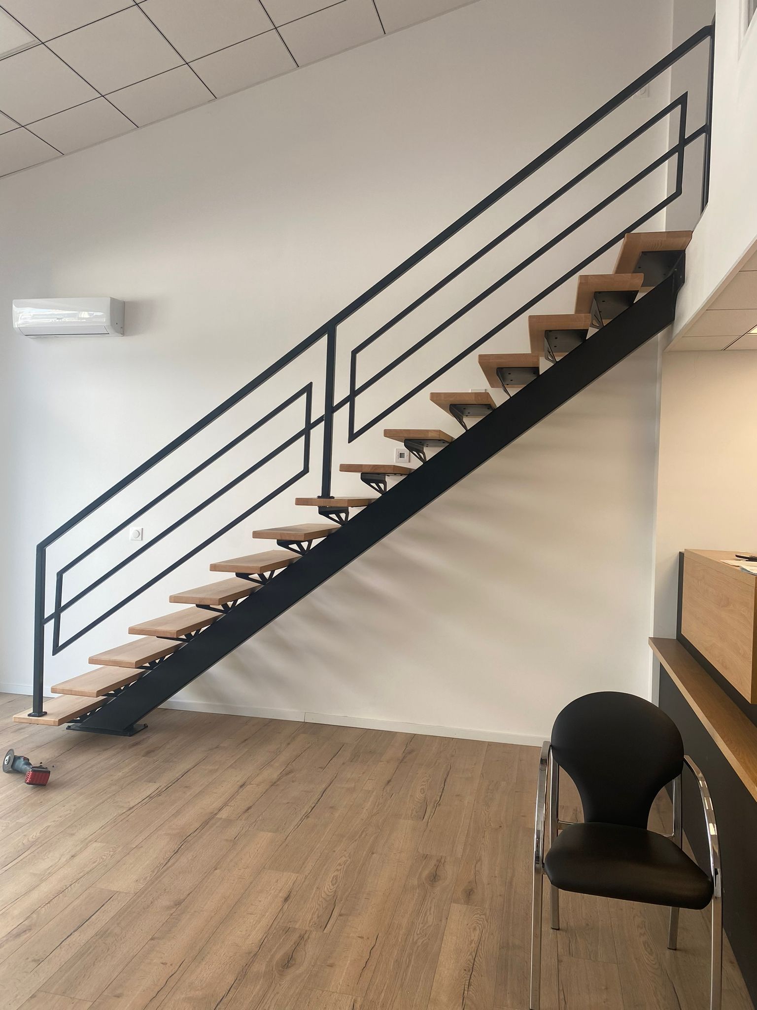 Escalier en métal noir avec marches en bois, rampe noire, murs blancs et plancher en bois.