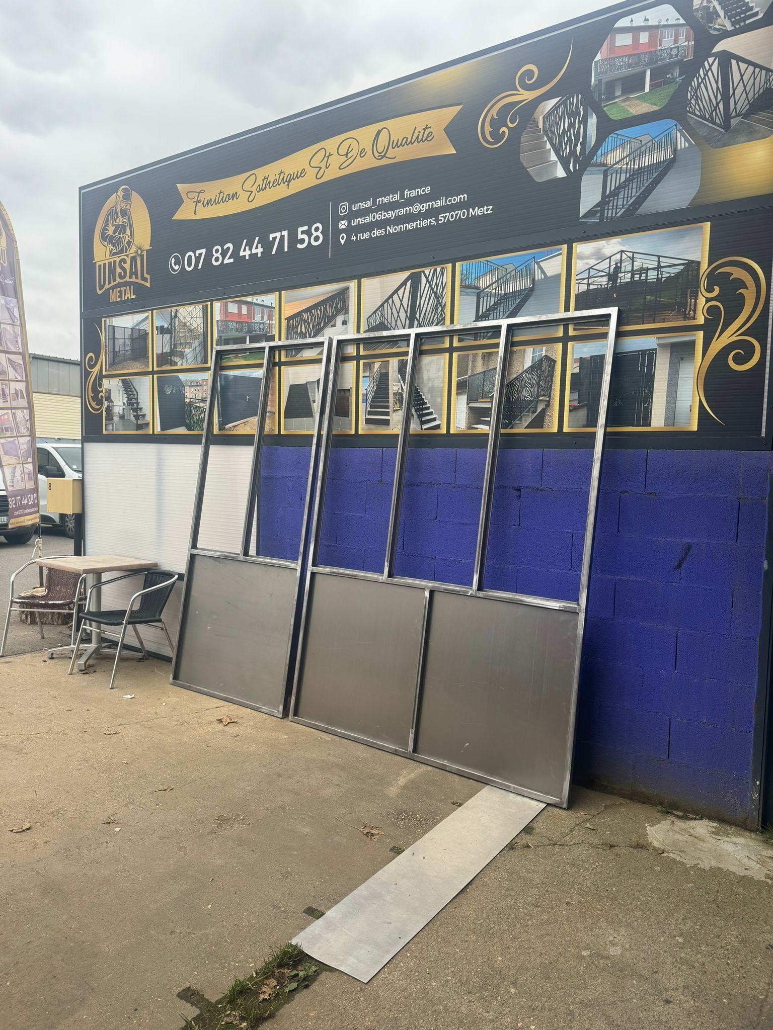 Trois panneaux à cadre métallique étaient appuyés contre un mur bleu. Une enseigne de magasin se trouvait derrière les panneaux.