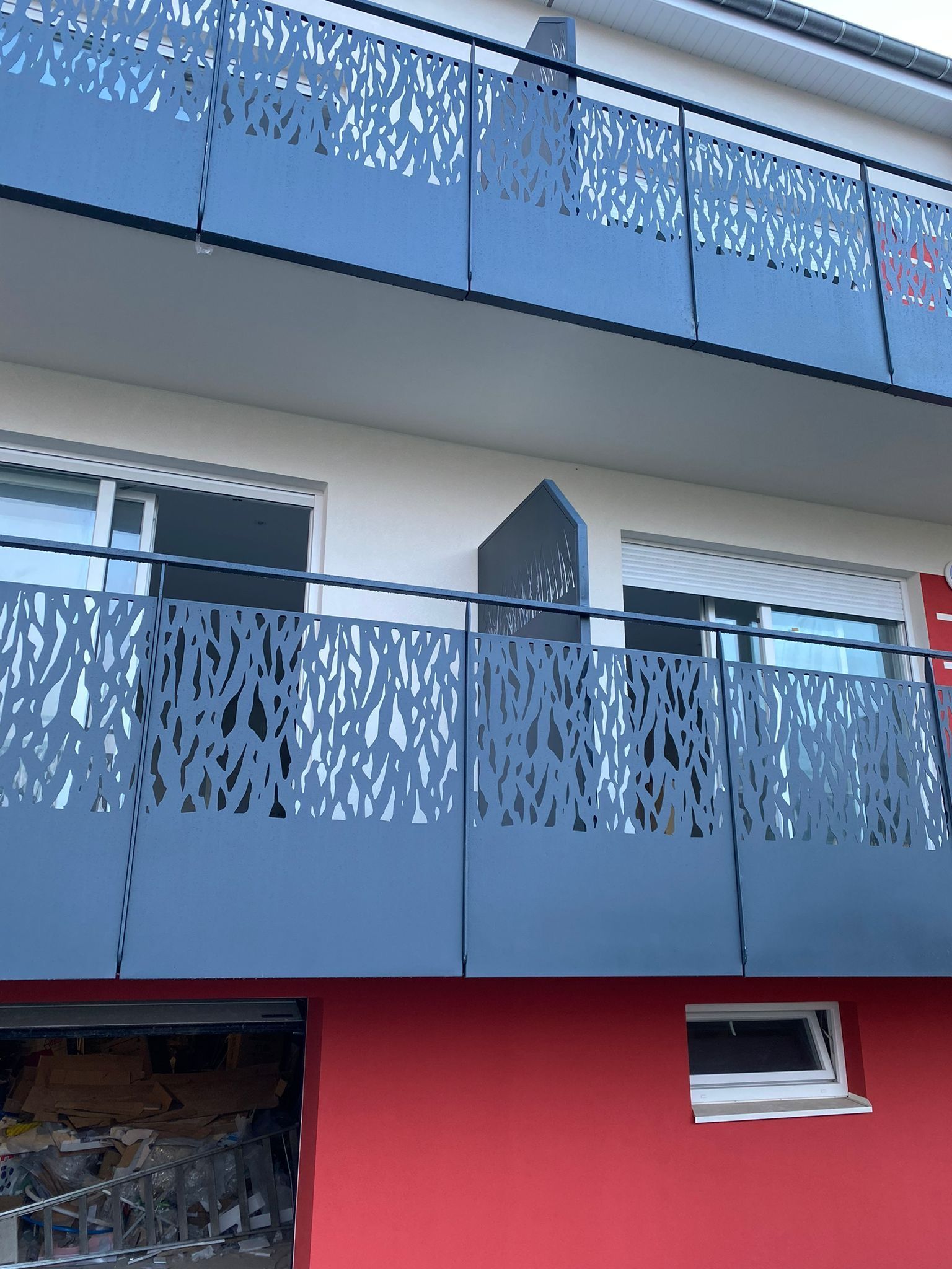 Balcon orné de panneaux métalliques décoratifs découpés au laser, devant un bâtiment aux murs rouge et blanc.
