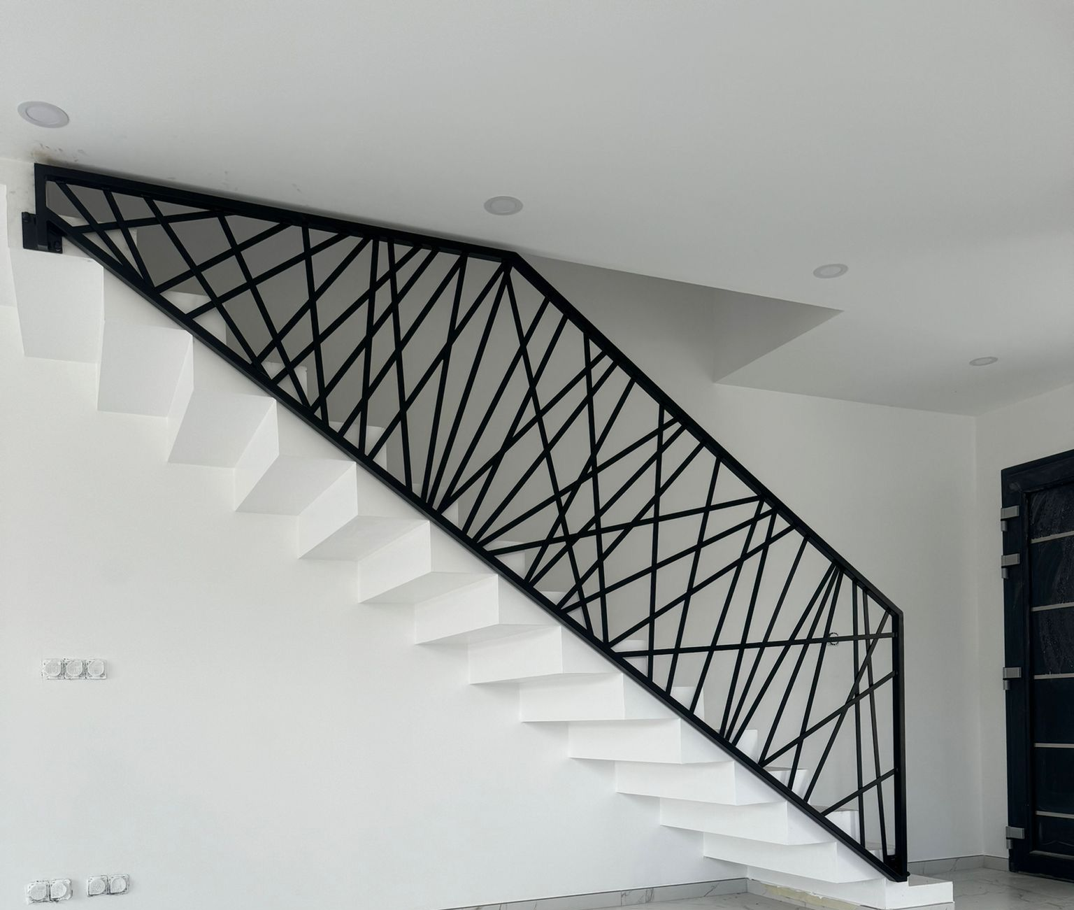 Rambarde géométrique en métal noir sur un escalier blanc.