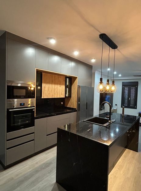 Cocina moderna con gabinetes grises, encimeras negras e isla con luces colgantes.