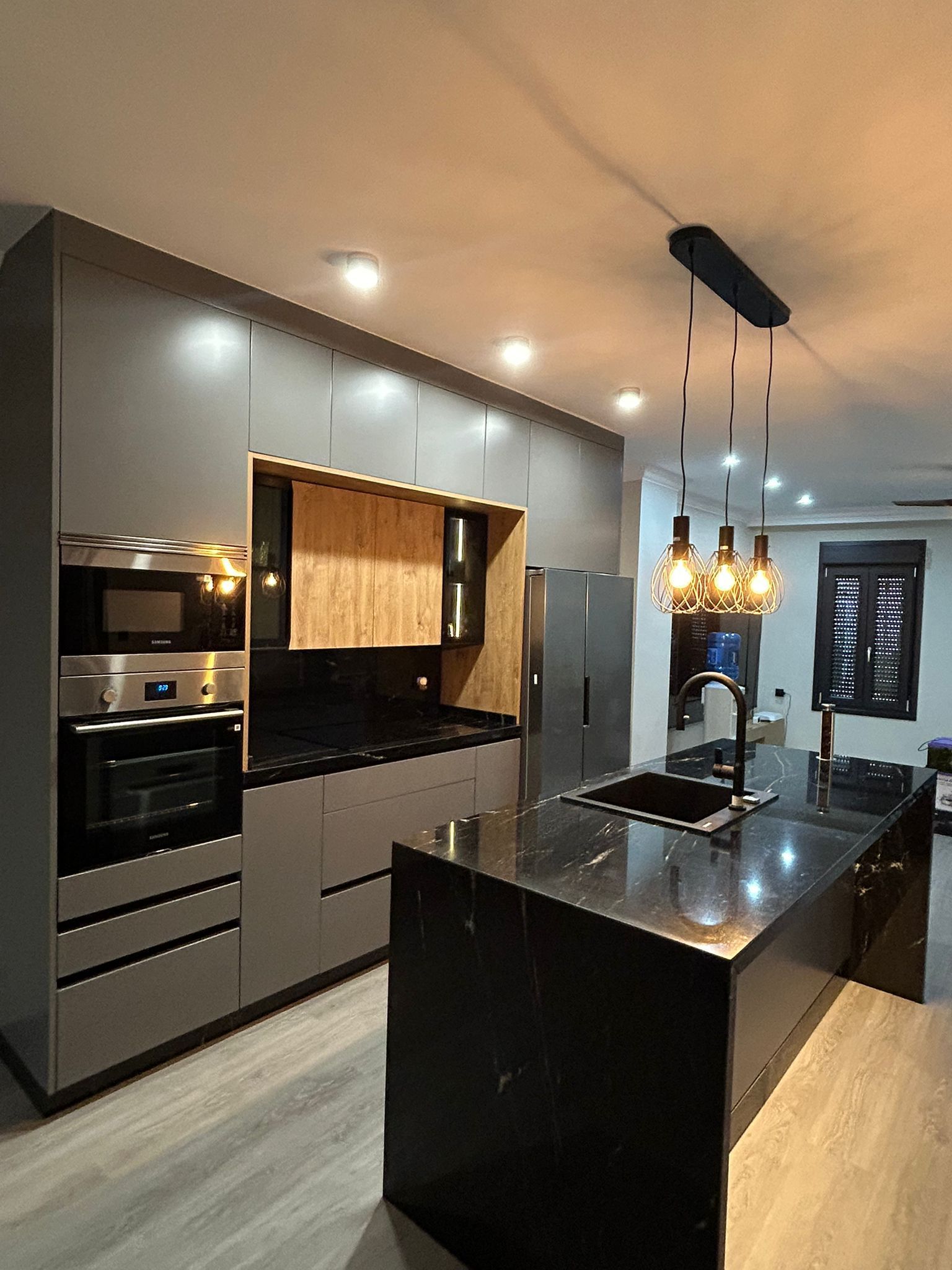 Cocina moderna con gabinetes grises, encimeras negras e isla con luces colgantes.