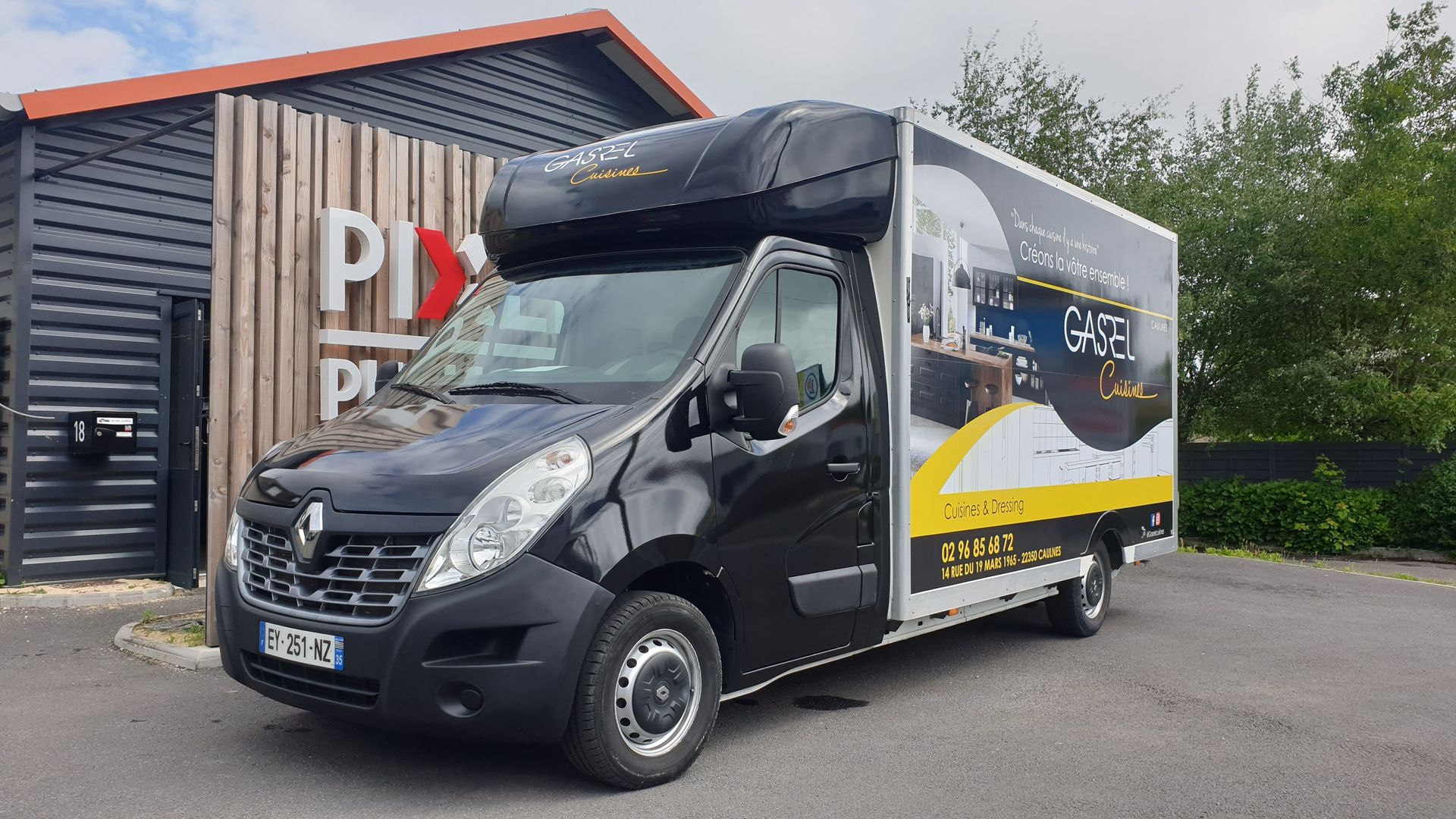 Camionnette de livraison noire garée devant un bâtiment avec un panneau. La camionnette affiche une publicité sur le côté.