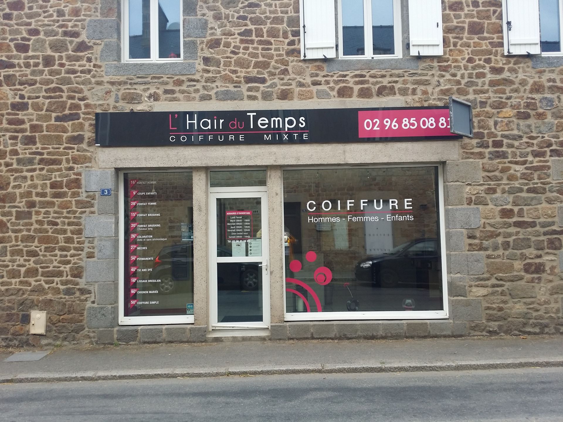 Salon de coiffure L'Hair du Temps dans un immeuble en pierre avec de grandes vitrines en façade.