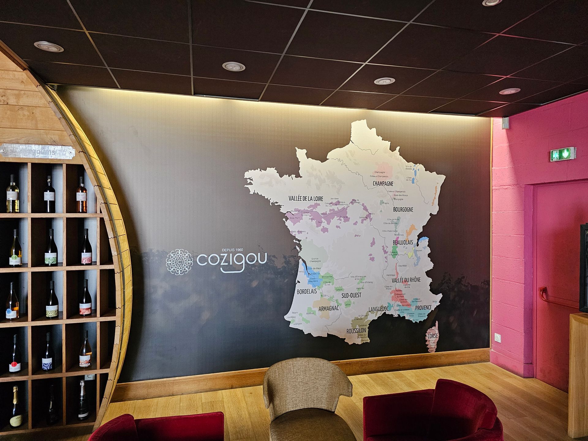 Intérieur d'une cave à vin. Carte de France présentant les régions viticoles, avec des bouteilles exposées dans un présentoir en bois.