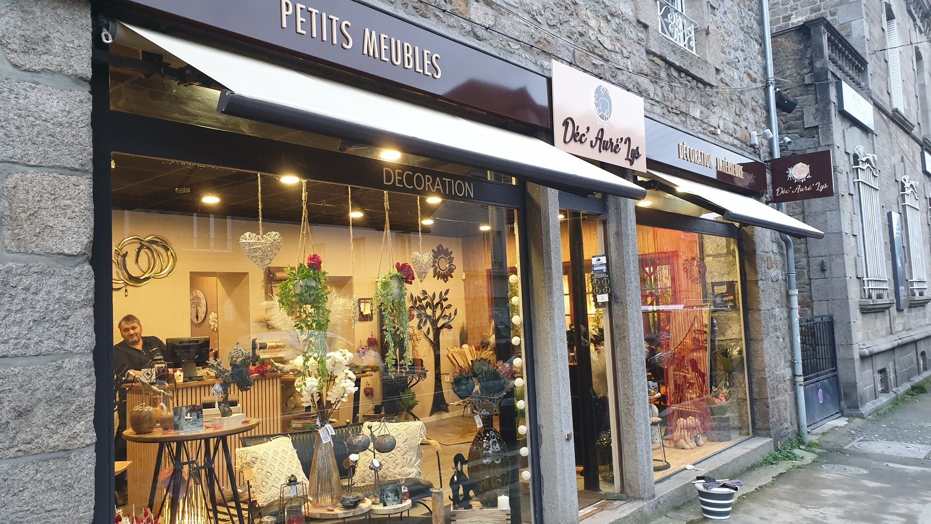 Devanture : Petits Meubles avec décor et marchandises exposées dans des vitrines sur une façade en pierre.