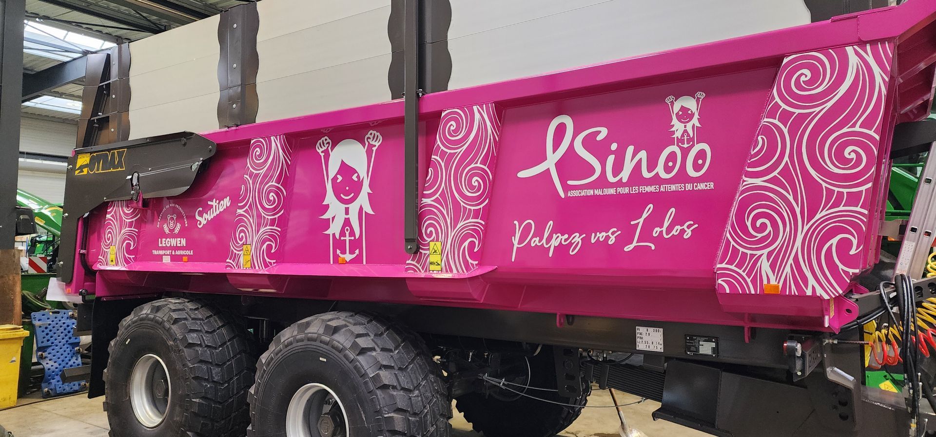 Camion à benne rose avec logos et tourbillons décoratifs, garé à l'intérieur.