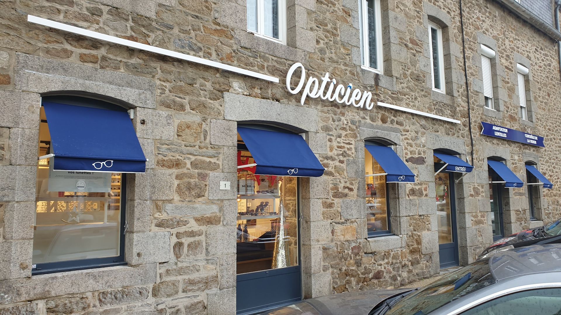 Bâtiment en pierre avec auvents bleus ; devanture d'un opticien français.