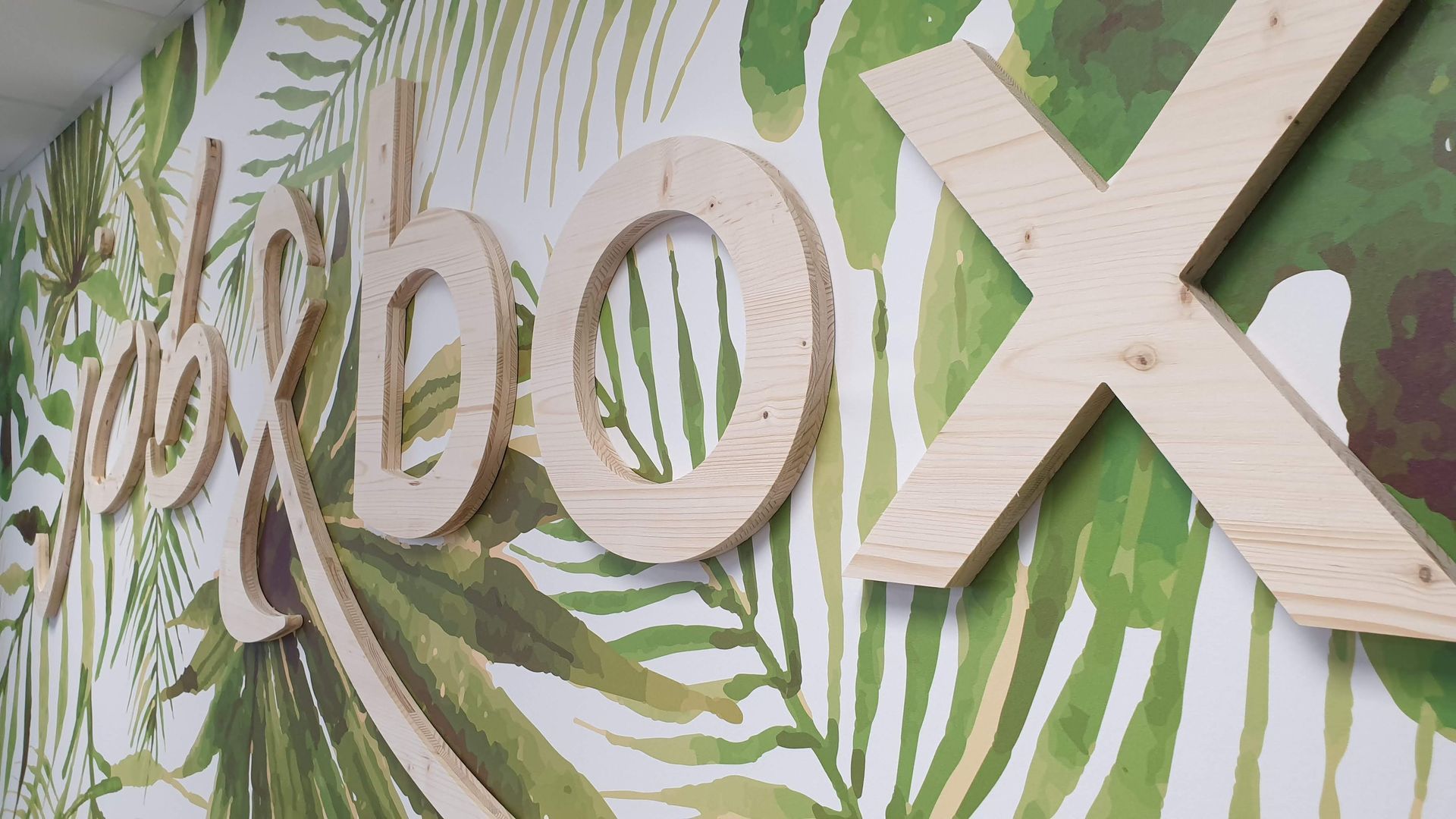 Lettres  job & box en bois sur un mur avec un motif de feuilles vertes et blanches.