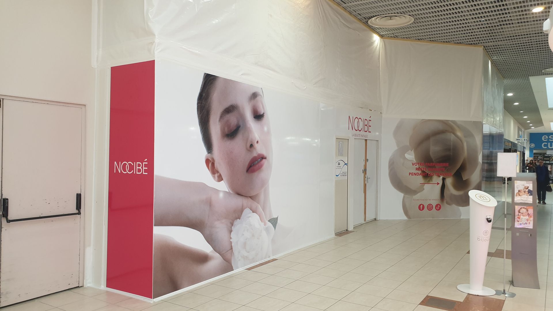 Couloir avec publicité représentant une femme appliquant un soin. Couleurs rouge et blanc.