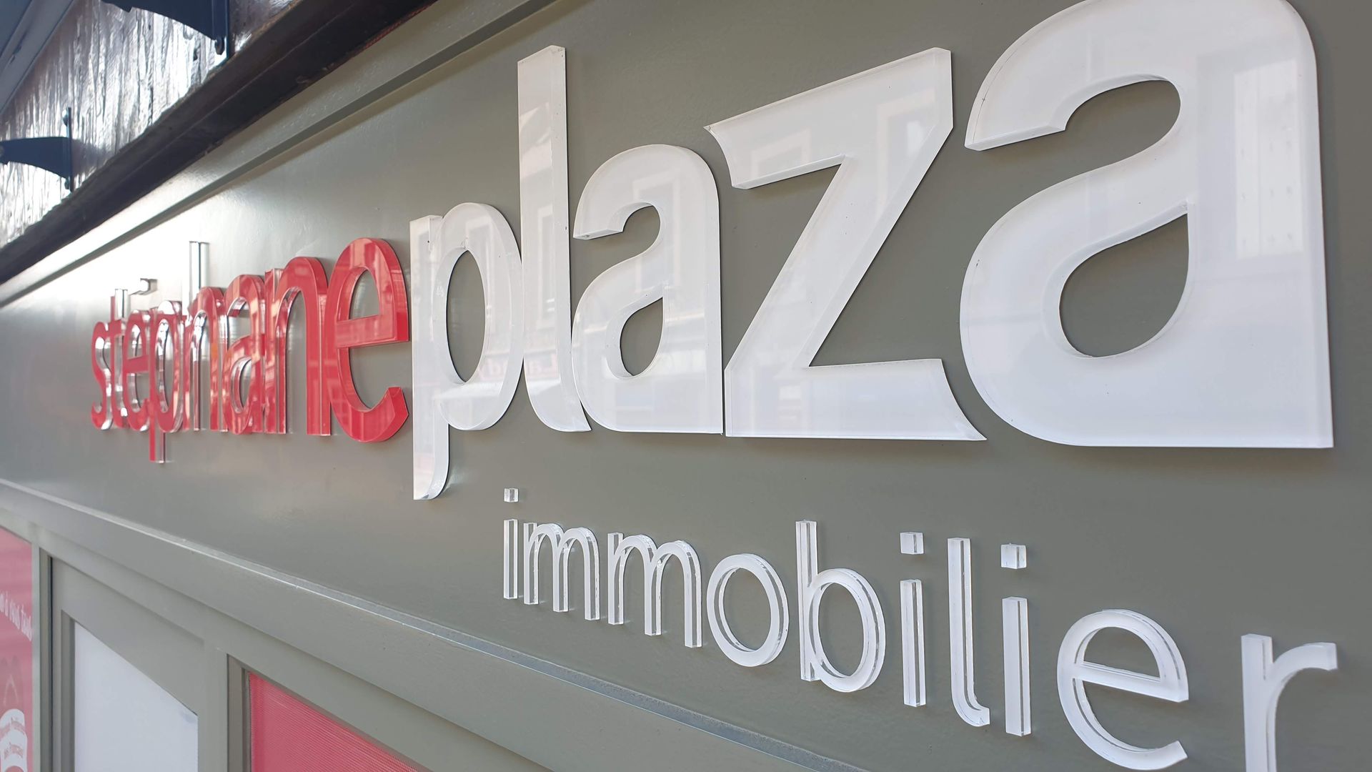 Panneau pour Stéphane Plaza immobilier, lettres rouges et blanches sur un bâtiment gris.