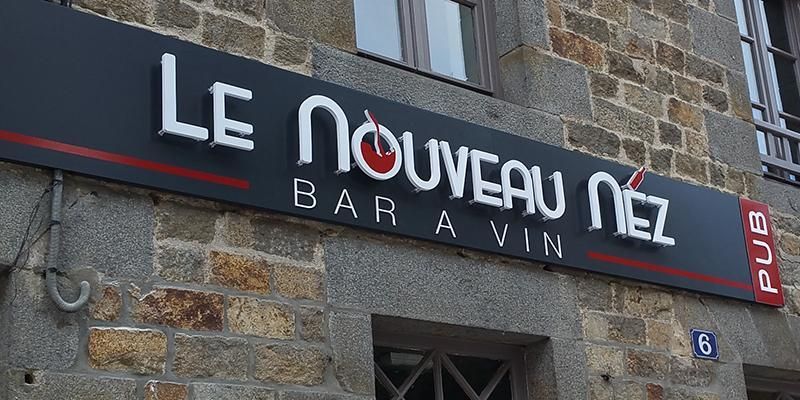 Enseigne Le Nouveau Nez (bar à vin) sur un bâtiment en pierre. Avec horloge et inscription pub.