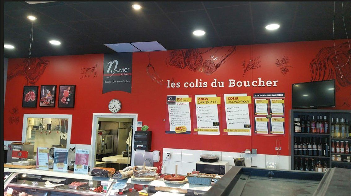Intérieur de boucherie avec mur rouge, menus, comptoir d'exposition et produits à vendre.