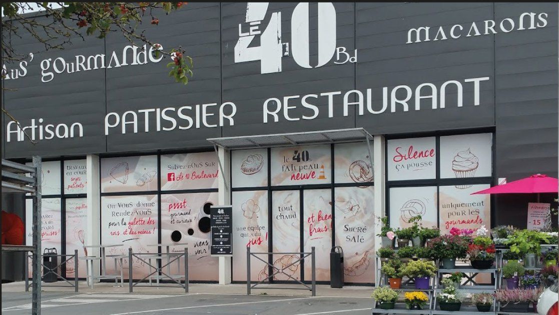 Une façade de restaurant avec un grand panneau 40 , le texte PATISSIER RESTAURANT et des vitrines avec des affichages de menus ; des fleurs devant.