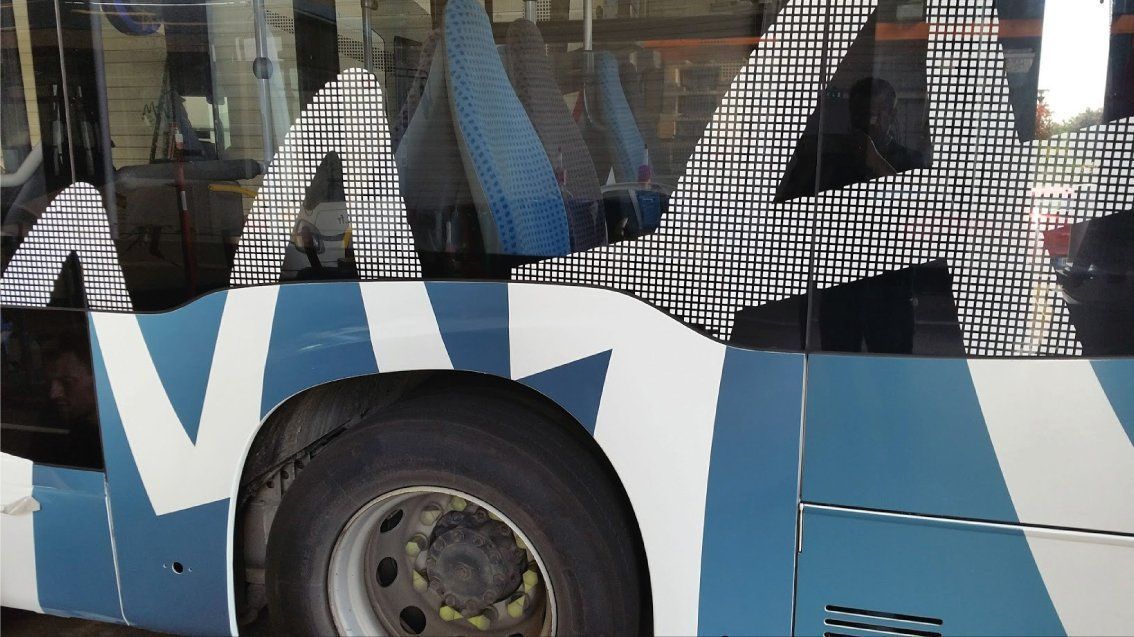 Bus bleu et blanc avec camouflage noir et blanc sur les vitres et les panneaux latéraux. Un gros pneu est visible.