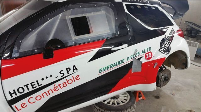 Une voiture de course partiellement démontée, accents rouges et noirs, avec logos de sponsors, dans un garage.
