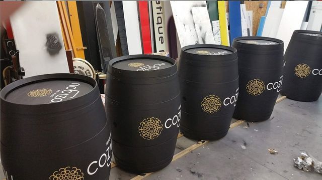 Cinq barils décoratifs noirs avec des logos dorés sur une table.