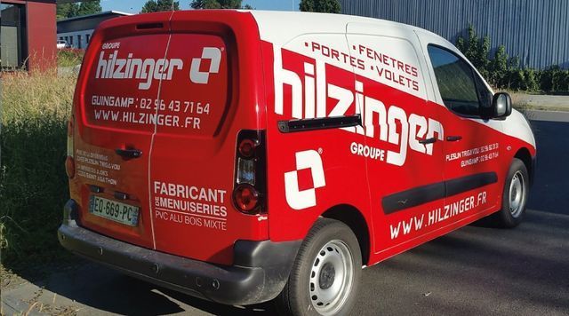 Fourgonnette Hilzinger rouge et blanche. Logo et coordonnées sur le côté.