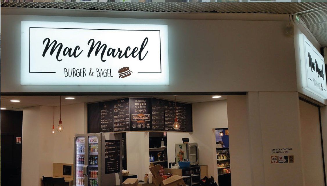 Devanture du café Mac Marcel avec enseigne rétroéclairée.