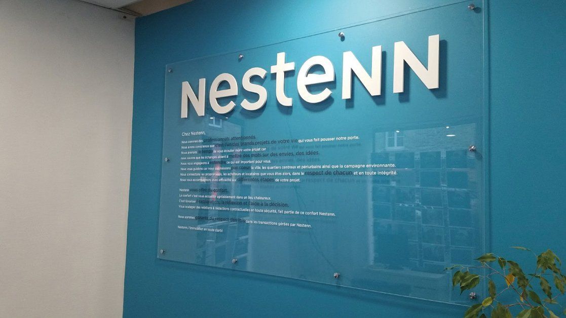 Panneau avec le logo Nestenn sur un mur bleu avec du texte en dessous.