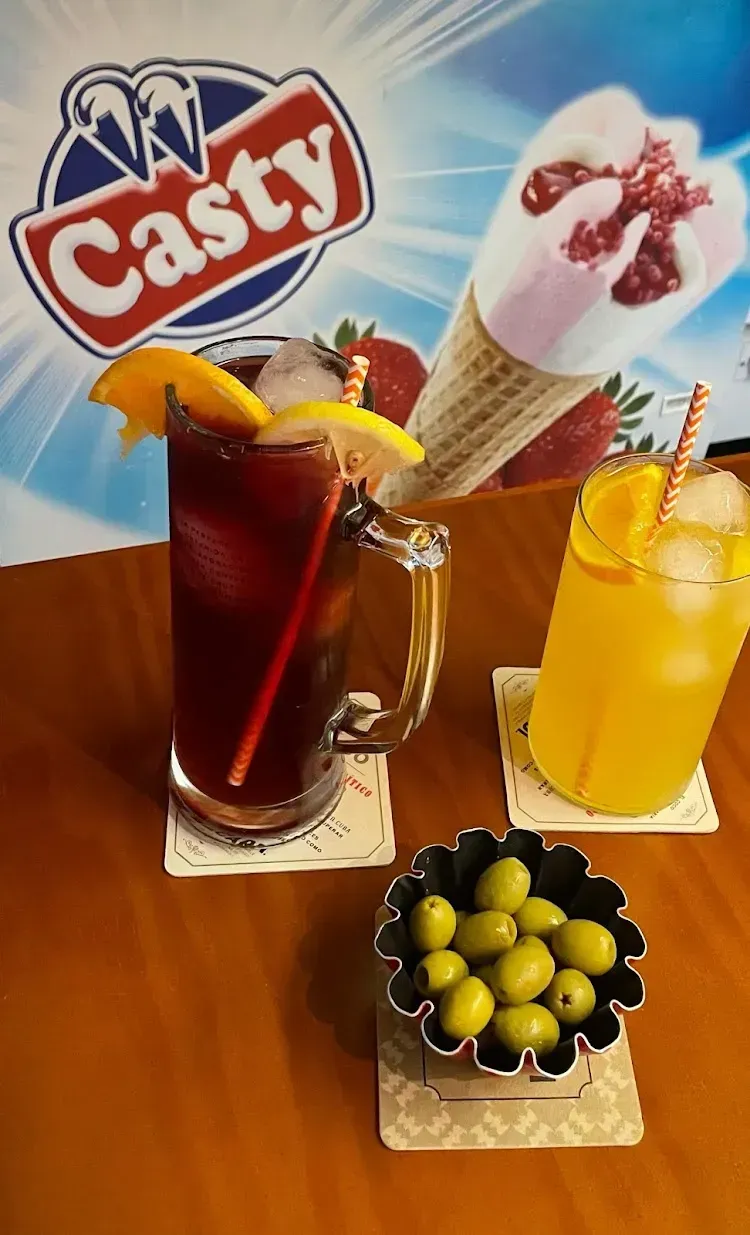 Dos bebidas, una roja y otra naranja, con hielo, guarnición de frutas y un bol de aceitunas verdes.
