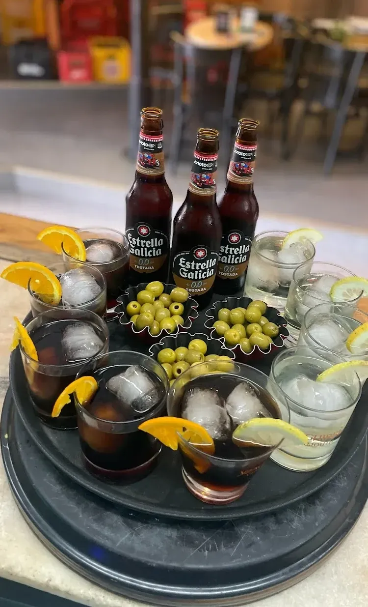 Una bandeja con cervezas Estrella Galicia, cócteles con rodajas de naranja, aceitunas y hielo en un ambiente de bar.