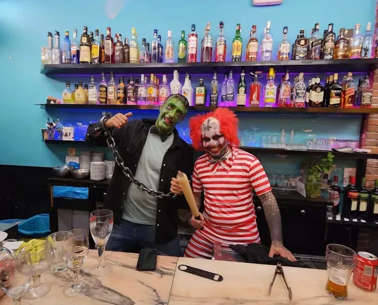 Dos personas disfrazadas de Halloween en un bar. Una vestida de Frankenstein y la otra de payaso. 