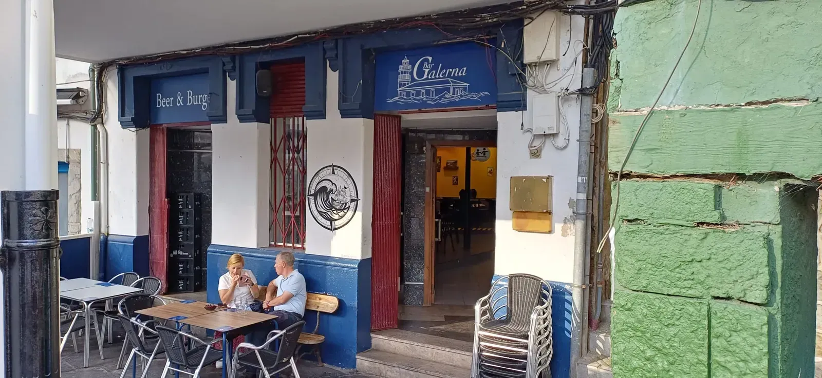 Edificios coloridos en una ladera de un pueblo costero, con un bosque al fondo y un cielo nublado.